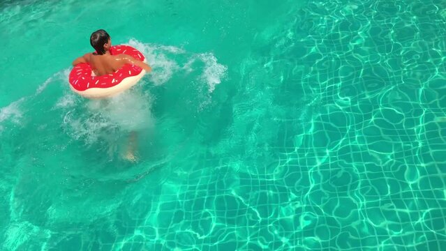 Young adult jumping in the pool with inflatable swim doughnut.