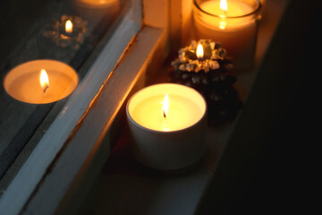 Lit candles and Christmas decorations on the window sill at night. Hygge at home. Selective focus.