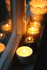 Lit candles and Christmas decorations on the window sill at night. Hygge at home. Selective focus.
