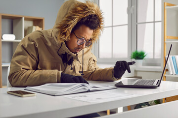 Freezing African American man working at laptop computer in office. African American man wearing...