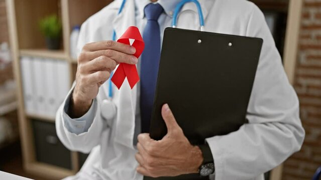 Young hispanic man doctor holding red ribbon and clipboard at the clinic