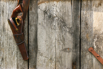 A black powder revolver in a leather holster hangs on a leather belt on the background of old, worn...