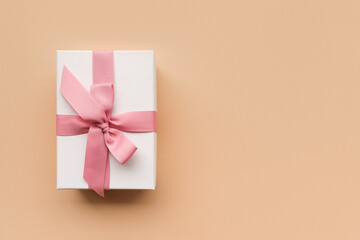 White gift box with a pink ribbon on a peach background, top view. New Year, Christmas, St....