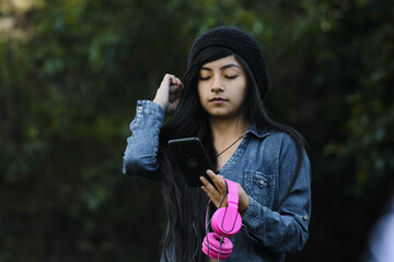 Joven atractiva parado con auriculares mirando la pantalla de  su celular en las manos, teléfono...