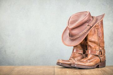 Vintage cowboy hat and old leather Wild West boots front concrete wall background. Retro style...