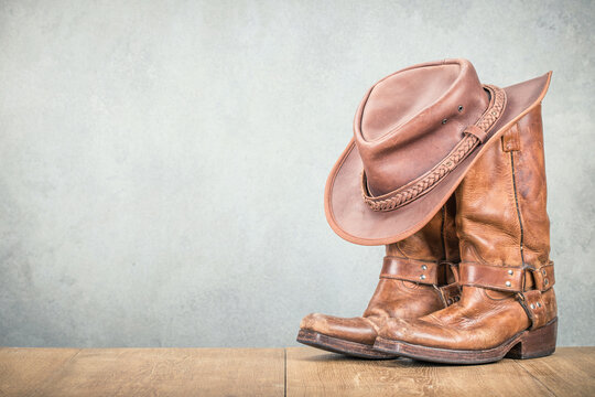 Vintage cowboy hat and old leather Wild West boots front concrete wall background. Retro style filtered photo