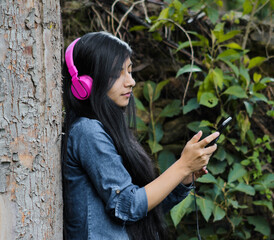 Mujer joven atractiva con auriculares disfrutando de música o un podcast en el parque o bosque,...