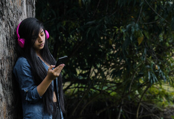 Mujer joven atractiva con auriculares disfrutando de música o un podcast en el parque o bosque,...