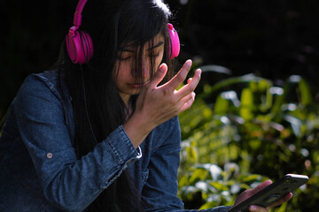 Mujer joven atractiva con auriculares disfrutando de música o un podcast en el parque o bosque,...