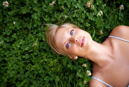 Spring, thinking and relax with woman on grass in nature for calm, environment and peace. Park, flowers and field with face of female person lying in countryside for summer, vacation and wellness