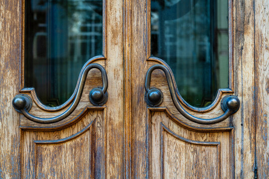 Dark old brown doors with bronze handles and glass. Wooden door with windows with street reflection, closeup