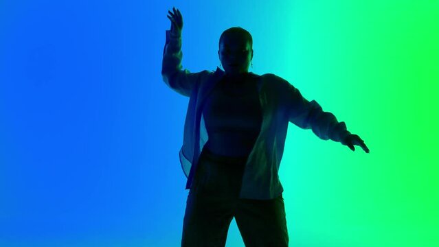 Silhouette of a woman dancing jazz-funk on green and blue neon background in a studio. Modern dynamic and energetic dance choreography. Medium full.