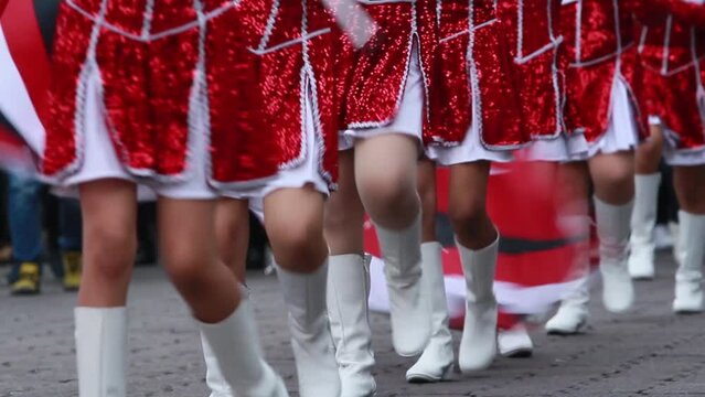 Close up legs, teen cheerleaders with red bright dress and white boots marching on a parade weaving red and white flags