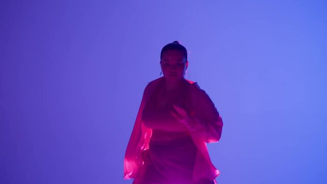 Attractive woman dancing jazz-funk in pink and blue neon light in a studio. Modern dynamic and energetic dance choreography. Medium full.