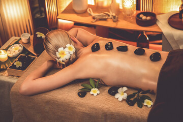 Obraz na płótnie Canvas Hot stone massage at spa salon in luxury resort with warm candle light, blissful woman customer enjoying spa basalt stone massage glide over body with soothing warmth. Quiescent