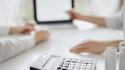 Calculator is lying at the white table near two female accounters counting taxes or making revenue balance. Business audit and finance concepts