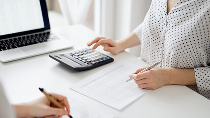Two accountants using a calculator and laptop computer for counting taxes or revenue balance while rolls of receipts are waiting to be calculating. Business audit and taxes concepts