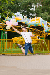Funny guy holds a bunch of balloons in his hands at amusement park b bounces up having fun