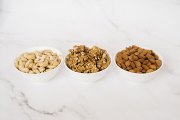 Cashew, walnut and almonds in white cups on a marble table