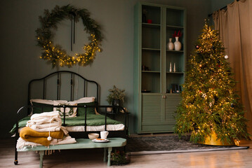 Interior of a cozy bedroom with a bed and a wreath on the wall, a Christmas tree without toys with lights
