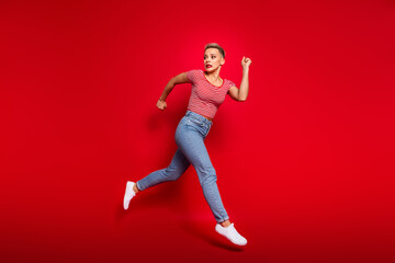 Full length photo of stressed girl wear stylish striped clothes running away looking empty space isolated on red color background