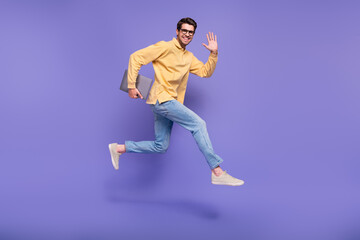Full body photo of jump run young businessman wear yellow trendy shirt waving palm hi word with laptop isolated on violet color background