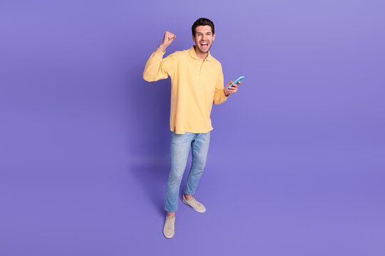 Full body photo of crazy shouting young guy fist up victory jackpot betting parimatch website phone app isolated on violet color background