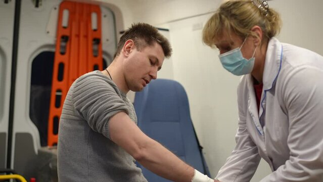 A paramedic in an ambulance applies a soft gauze bandage to the man's right wrist, while the man is in severe pain
