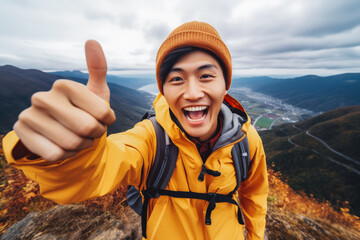Naklejka premium Young chinese hiker man taking a selfie portrait on the top of a mountain. Happy young athletic man on a adventure, taking a photo with beautiful view