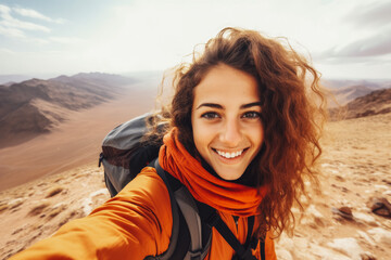 Fototapeta premium Young arab hiker woman taking a selfie portrait on the top of mountain. Happy young athletic woman on adventure, taking a photo with beautiful view
