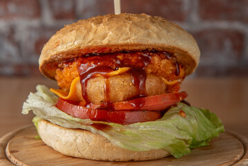 vegan burger with cheddar and barbecue sauce centred on a wooden plate on a brick wall background, 