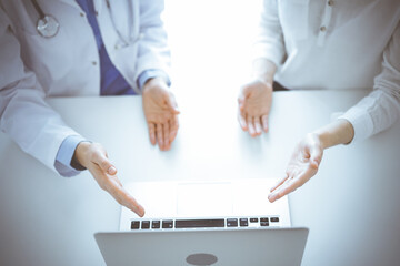 Doctor and patient sitting near each other at the table in clinic. The focus is on female hands pointing into tablet computer touchpad together. Medicine concept
