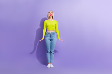 Fototapeta na wymiar Full length photo of optimistic gorgeous woman dressed yellow clothes jeans look at offer empty space isolated on purple color background