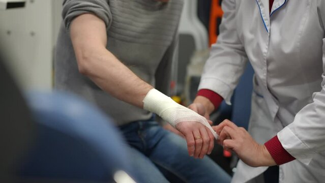A paramedic applies a soft gauze bandage to the right wrist of a man sitting in an ambulance
