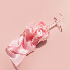 Creative aesthetic pastel pink composition with champagne glass and satin fabric, party time.