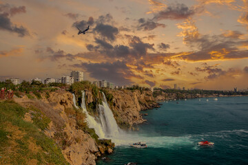 The moment when the Lower Düden waterfall flows into the sea, against the background of the steep shores of the Mediterranean and the urban development of the city of Antalya.