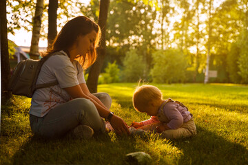 Mother plays with cute blonde baby toddler in the park at sunset. The concept of a happy childhood,...
