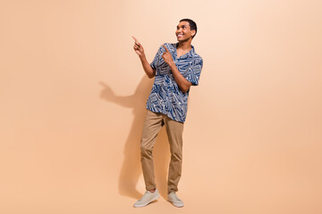 Full length photo of funky dreamy guy dressed print shirt pointing two fingers empty space isolated beige color background