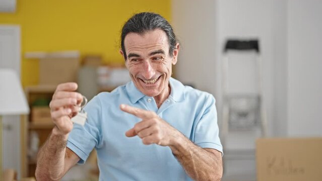 Middle age man pointing to new house keys doing thumb up gesture at new home