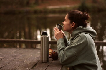 young woman smiling drinking tea from thermos with muffin outdoors