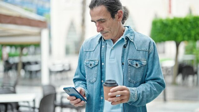 Middle age man using smartphone drinking coffee smiling at coffee shop terrace
