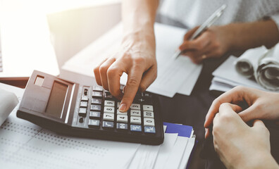 Woman accountant using a calculator and laptop computer while counting taxes for a client. Business...