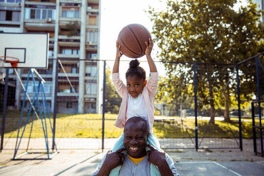 Happy little girl having fun with her grandpa on a basketball court