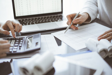 Woman accountant using a calculator and laptop computer while counting taxes for a client. Business...