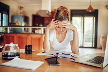 Concerned young woman reading through bank statements at home - obrazy, fototapety, plakaty