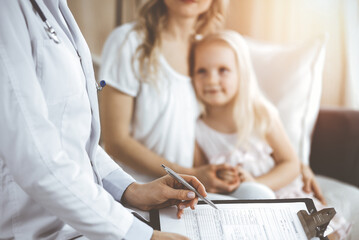 Doctor and patient. Pediatrician using clipboard while examining little girl with her mother at home. Happy cute caucasian child at medical exam. Medicine concept - 668842085