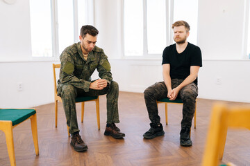 Front view of bearded Caucasian soldier male suffering depression sharing thoughts with group of people sitting in circle during PTSD group therapy session. Concept of mental health, depression.