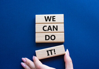 We can do it symbol. Concept words We can do it on wooden blocks. Beautiful deep blue background. Businessman hand. Business and We can do it concept. Copy space. - obrazy, fototapety, plakaty