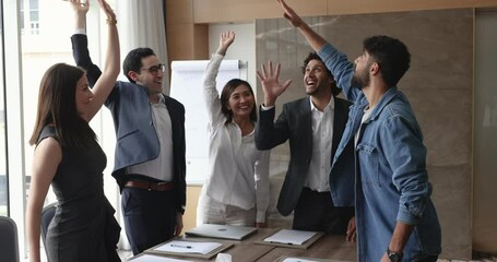 Happy multinational young team celebrate business success stack their hands together at group meeting enjoy corporate victory, great teamwork results, engaged in teambuilding event in conference room