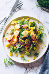 Healthy salad with fresh vegetables - corn, avocado, red onion, shrimp and coriander on a white plate.